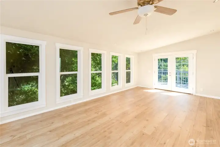 Expansive living room with floor-to-ceiling windows, French doors to the deck, and peaceful woodland views.