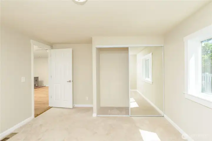 Second bedroom with carpet, mirrored closet doors, and natural light.