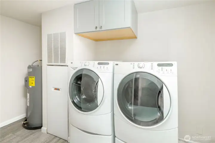 A dedicated laundry area with full-size front-loading washer and dryer, overhead storage cabinets, durable tile flooring, and convenient access, making everyday chores simple and organized.