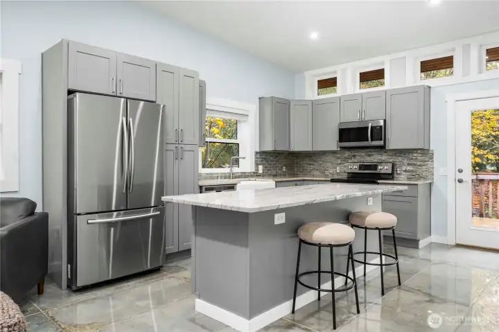 The kitchen offers a huge island with barstool seating, quartz countertops, and stainless steel appliances for a stylish setting any chef would love. An adjoining deck perfect for entertaining looks out over the front yard. A primary suite—one of two in this home—comes with it’s own bath and opens out to the deck. A