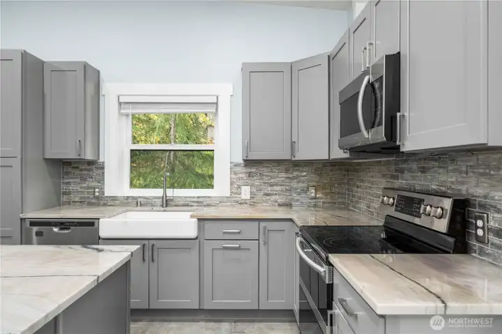 The kitchen offers a huge island with barstool seating, quartz countertops, and stainless steel appliances for a stylish setting any chef would love. An adjoining deck perfect for entertaining looks out over the front yard. A primary suite—one of two in this home—comes with it’s own bath and opens out to the deck. A