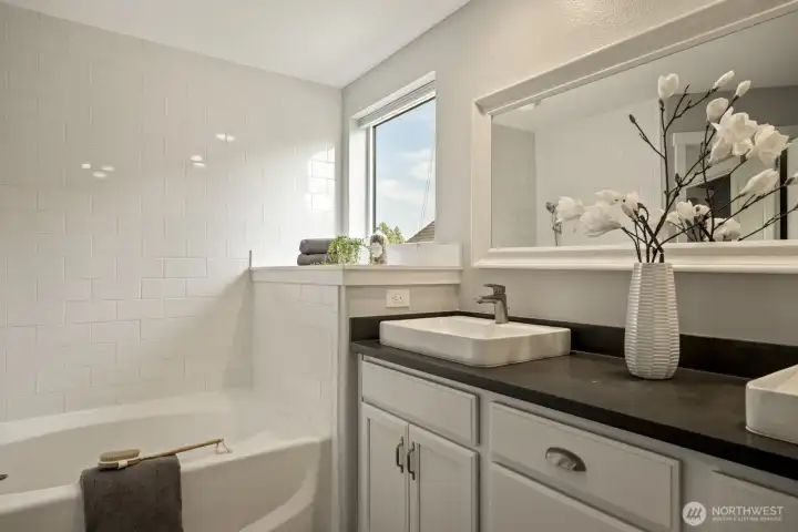 Beautiful primary bath featuring a modern double-sink vanity, a generous soaking tub with a subway-tile accent wall, and an expansive shower with dual shower heads.