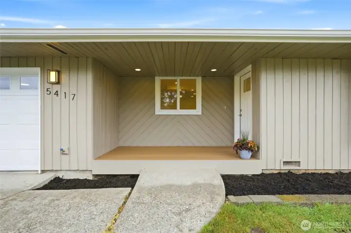 Covered front porch entry features durable composite decking, modern recessed lighting, and a modern, weather-protected front door.