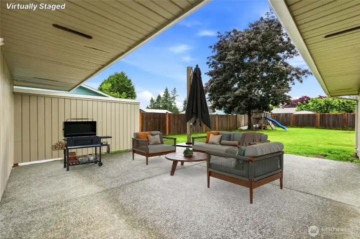Expansive covered concrete patio provides an ideal year-round outdoor entertainment space, overlooking a vast, fully fenced level backyard.