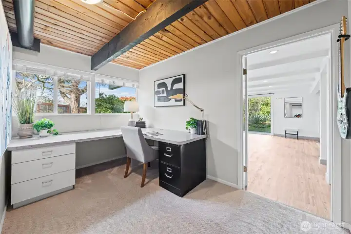 Dedicated workspace with built-in desk, expansive counter surface, and large windows for natural light. Wood ceiling with exposed beams adds character, creating an inspiring setting for work or study.