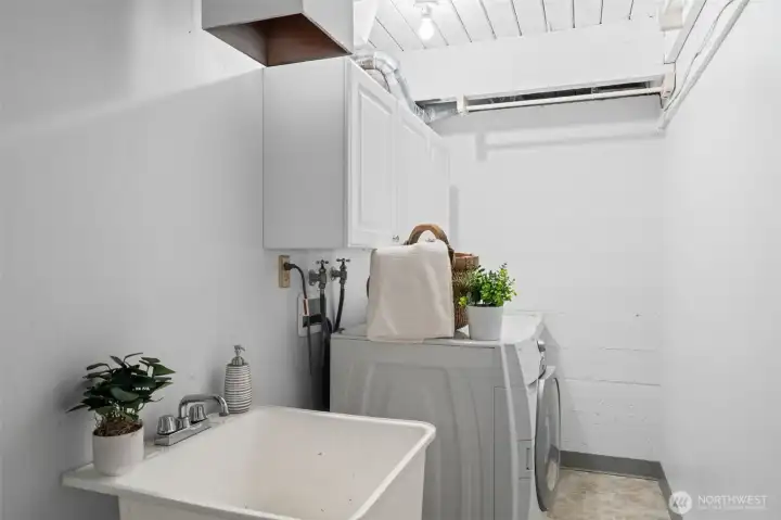 Functional lower-level utility space with washer and dryer, utility sink, and overhead storage. Practical layout offers room for laundry tasks, storage, and household organization.