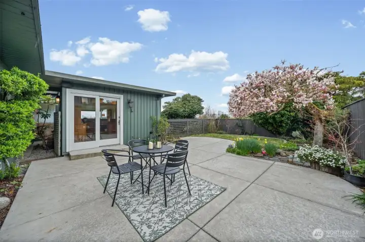 Inviting outdoor patio off the kitchen features ample space for dining and entertaining, surrounded by mature landscaping, blooming trees, and a fully fenced yard for privacy.