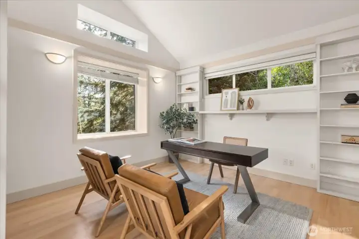 Elegant office/library featuring vaulted ceilings, new hardwood flooring (2026), built-in shelving, and a double-sided gas fireplace that enhances warmth and flow between spaces.