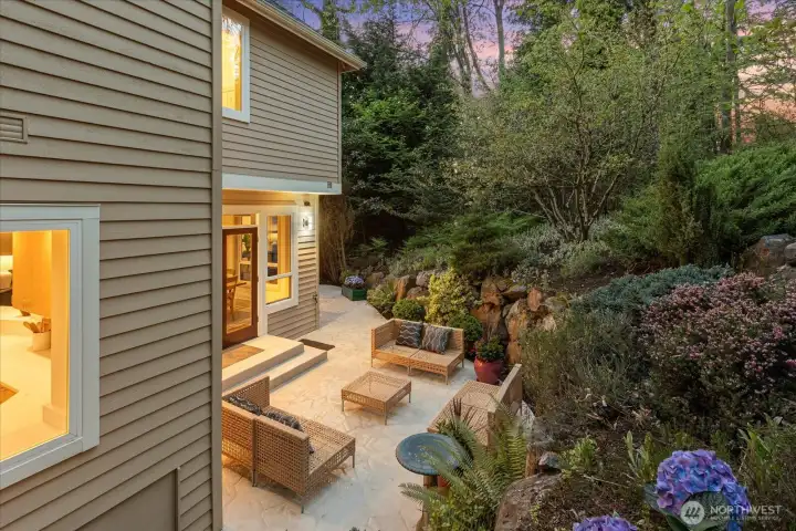 Serene outdoor retreat with lush landscaping, stone accents, and multiple seating areas—complete with outdoor speaker wiring for effortless ambiance.