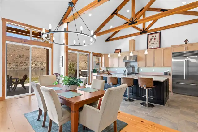 View 1 of the Living Room with soaring ceilings, exposed wood beams, wide plank wood floors, stone fireplace and glass sliding doors leading to the outdoor living area.