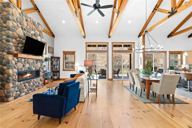View 2 of the Living Room with soaring ceilings, exposed wood beams, wide plank wood floors, stone fireplace and glass sliding doors leading to the outdoor living area.