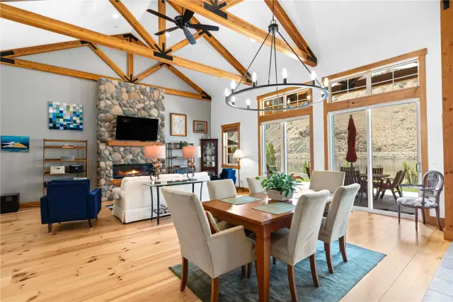View 3 of the Living Room and Dining Room with soaring ceilings, exposed wood beams, wide plank wood floors, stone fireplace and glass sliding doors leading to the outdoor living area.