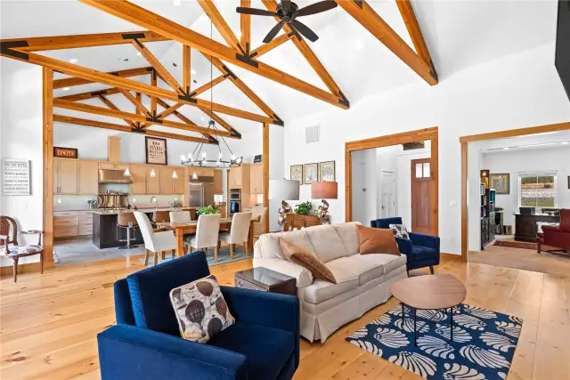 View 4 of the Living Room and Dining Room with soaring ceilings, exposed wood beams, wide plank wood floors, stone fireplace and glass sliding doors leading to the outdoor living area.