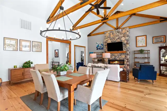 View 2 of the Dining Room with soaring ceilings, exposed wood beams, wide plank wood floors, stone fireplace and glass sliding doors leading to the outdoor living area.