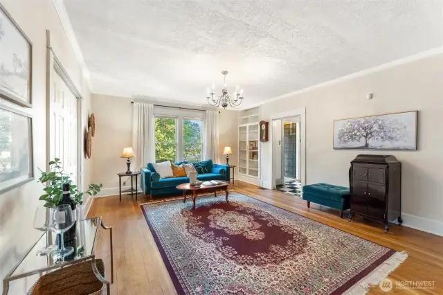 Open living room with expansive windows, chandelier lighting, and views of the surrounding greenery.