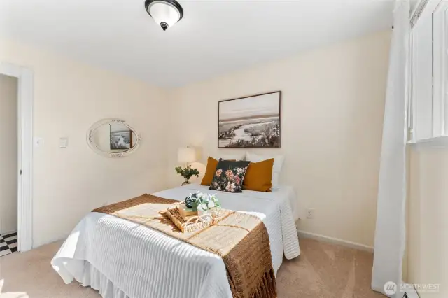 Main floor bedroom 2 (cont). Bright bedroom with soft carpet, natural light from a large window, and neutral tones for a warm, inviting feel.