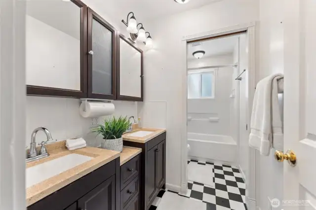 Updated main floor bathroom with dual sinks, rich cabinetry, and classic black-and-white flooring.