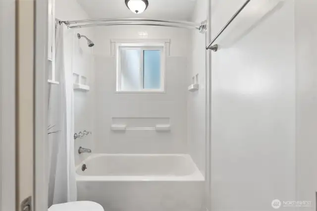 Bright bathroom with a tiled shower and tub combo, window for natural light, and timeless white finishes.