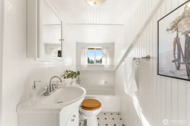 Bright upstairs bathroom with white beadboard walls, a tub/shower combo, and natural light from a large window.