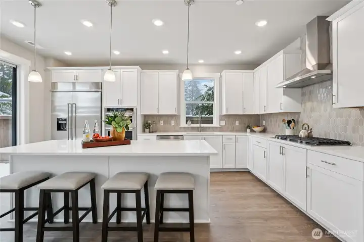 Gourmet kitchen featuring an expansive island, quartz countertops, 48" counter depth refrigerator, gas cooktop and built-in microwave and oven. Designed for both everyday living and entertaining. Showing another staged home in the community, white cabinetry is an upgrade.