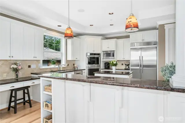 This spacious kitchen features abundant cabinetry, recessed and pendant lighting, quality stainless appliances, a desk area, and lake and mountain views.