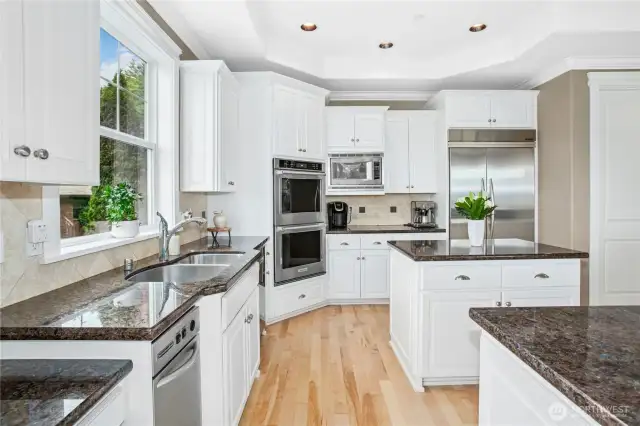 Another look at the kitchen shows the double ovens, slab granite countertops, and refinished hardwood floors.