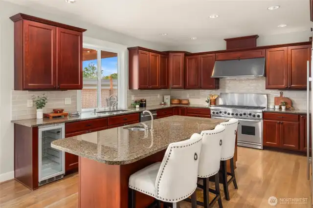 Oversized, polished kitchen with large island, numerous cabinets, beverage fridge, and stainless appliances.