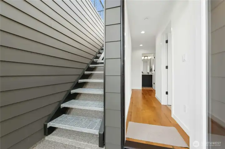 Exterior stairs to rooftop deck on left, third floor hallway on right, with door propped open.