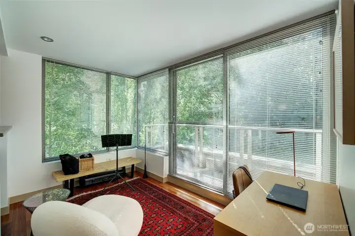 Den/office is light-filled with corner windows & trees.