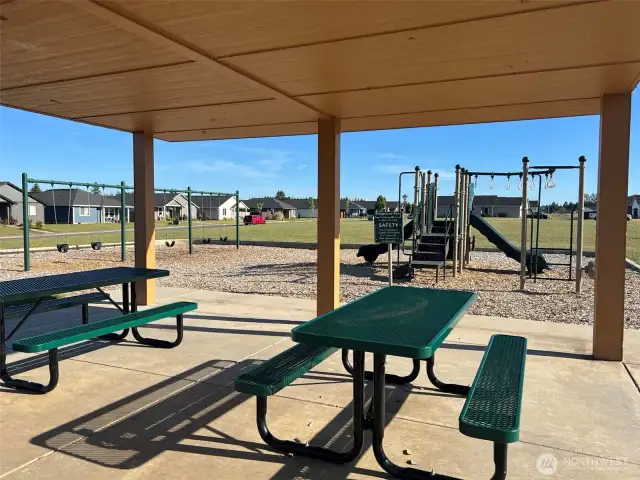 Private community park picnic area viewing playground, swings, and large field in background.