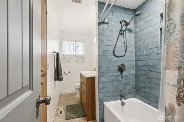 Meticulously maintained Des Moines home full bathroom, featuring striking glazed blue subway tile surrounds and a high-end contemporary rain shower system, perfectly complimented by a rich wood vanity and newer fixtures.