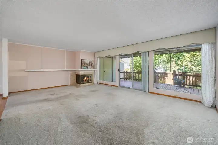 Large living area with a wood-burning fireplace and wall of windows to let the natural light indoors. Deck offers room for entertaining and flows into a private yard with mature landscaping - ready for some container gardening.