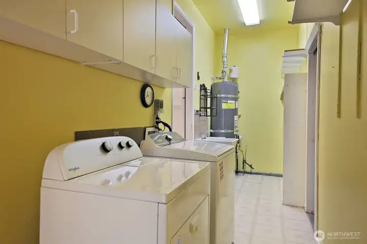 Located on the opposite end of the hallway (from the Primary Suite) is the laundry/utility room with extra storage and shelving and a hot water heater that has been replaced during current home ownership. There is a door to photographer's back that leads to the fenced portion of the yard. Door to the garage is along the right edge of this photo.