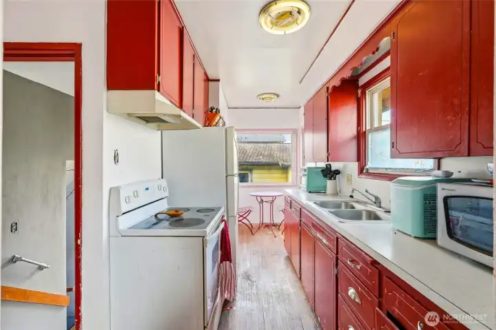 This vibrant galley-style kitchen offers plenty of cabinet storage, original wood floors, and a sunny breakfast nook overlooking the backyard.