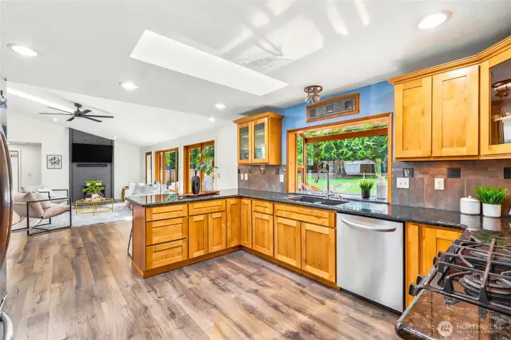 Well-appointed kitchen with granite countertops, gas range, stainless steel appliances, skylight, and backyard views.