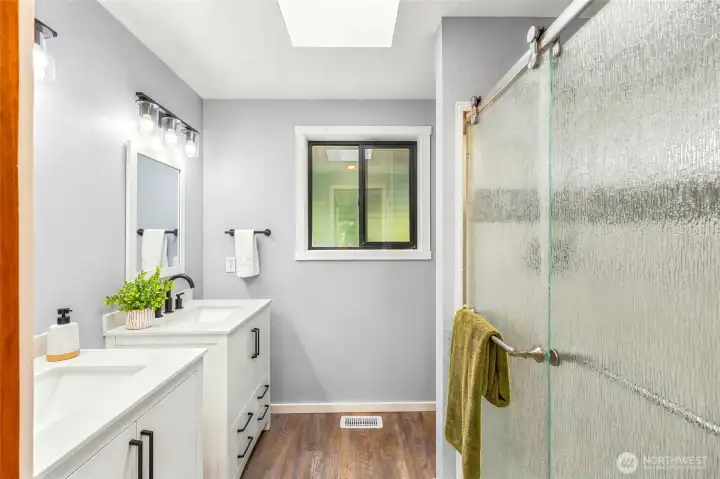 Beautifully renovated bathroom (2024) featuring dual vanities, updated cabinetry, modern fixtures, and a glass-enclosed shower.