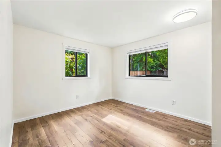 Bright bedroom featuring fresh paint, new laminate flooring, and peaceful views of the private backyard.