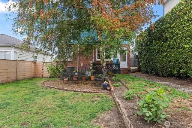 A garden-like backyard with a brick patio and mature hedges.