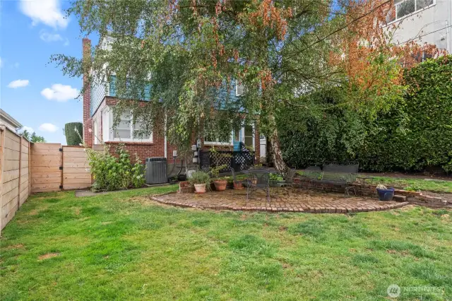 A garden-like backyard with a brick patio and mature hedges.