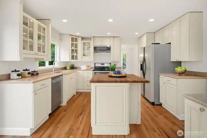 Expansive kitchen featuring a center island, abundant white cabinetry, stainless steel appliances, and hardwood floors, creating a bright and highly functional cooking space. Expansive kitchen featuring a center island, abundant white cabinetry, stainless steel appliances, and hardwood floors, creating a bright and highly functional cooking space.