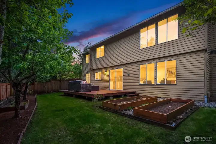 Stunning twilight exterior view highlighting the warmly lit home, spacious deck, and beautifully landscaped backyard, showcasing the perfect blend of indoor and outdoor living. Stunning twilight exterior view highlighting the warmly lit home, spacious deck, and beautifully landscaped backyard, showcasing the perfect blend of indoor and outdoor living.
