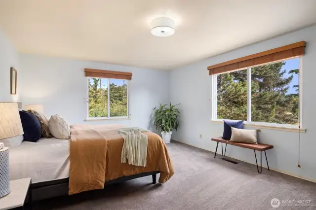 Primary bedroom with South East Facing windows that capture the morning light. offering a peaceful retreat with its ensuite room and views of the surrounding nature and balcony access.