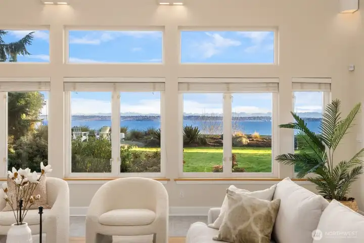 Large picture windows capture expansive water views and overlook the back lawn and firepit area, bringing natural light into the main living space.