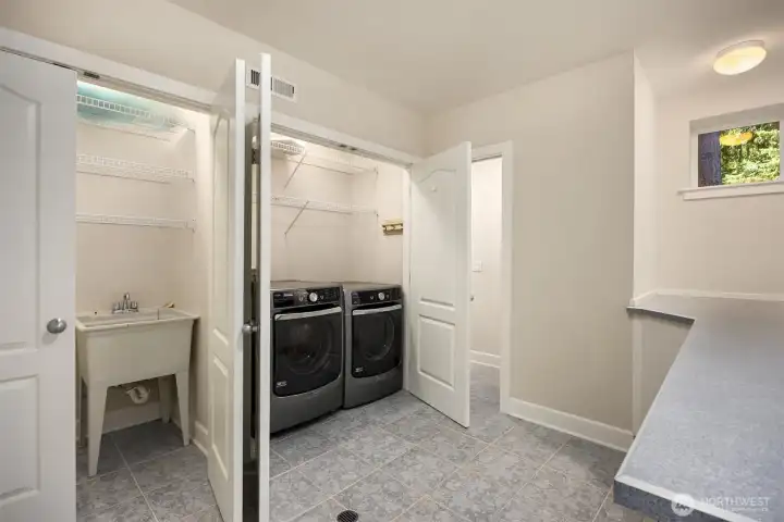 Downstairs dedicated laundry room with utility sink, front-loading washer and dryer, built-in shelving, and folding counter for added convenience. Connected to a half bath as well.