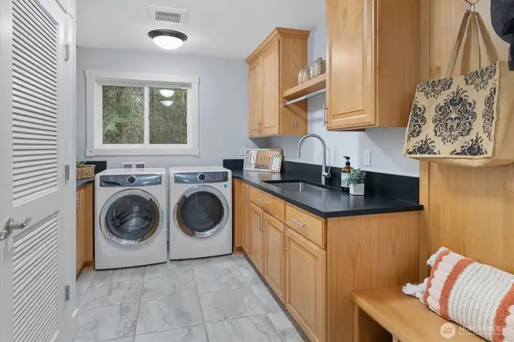 Utility room with sink and built in bench/storage/hanging hooks + closet. The black quartz extends throughout the home, including here.