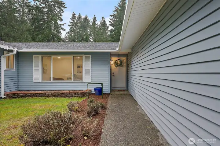 A welcoming concrete walkway leads to the front door, framed by manicured landscaping and classic white shuttered windows.