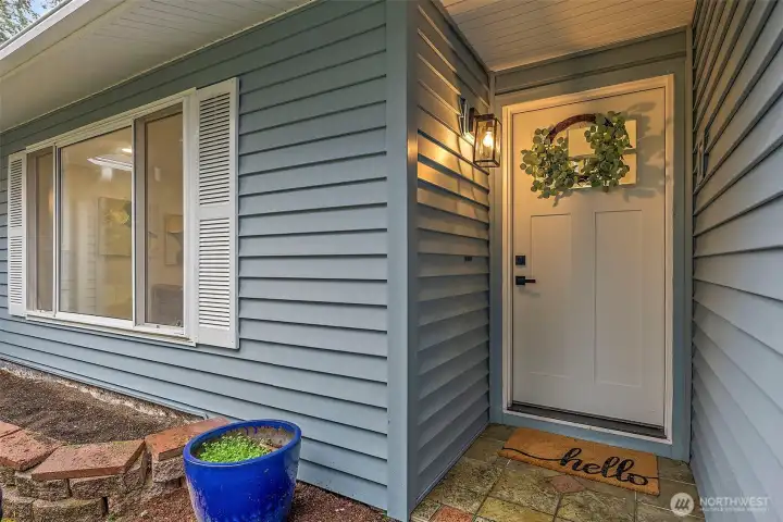The covered entry features a lantern wall sconce, decorative wreath, and stone tile landing — a warm first impression from the moment you arrive.