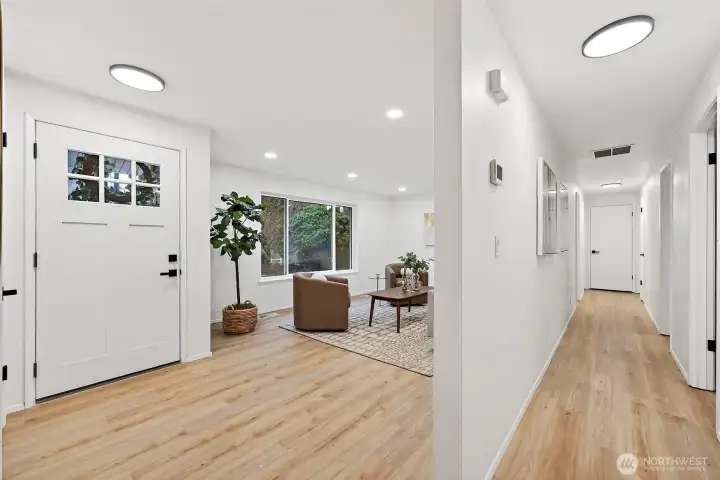 A striking craftsman-style front door with glass panel inserts and matte black hardware opens to the living area, with a wide hallway branching to the bedrooms beyond.
