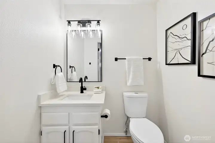 A crisp, updated bath features a white quartz vanity, matte black fixtures, framed mirror, and globe vanity lighting — clean and polished from top to bottom.