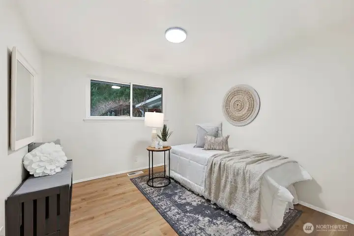 A well-proportioned secondary bedroom with LVP flooring, a window with treetop views, and a neutral palette ready to accommodate any layout or function.